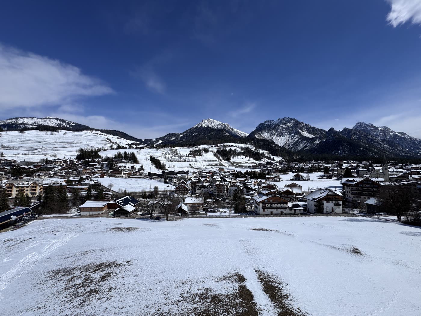 Snowy Dolomites village below mountain peaks seen from a ski slope